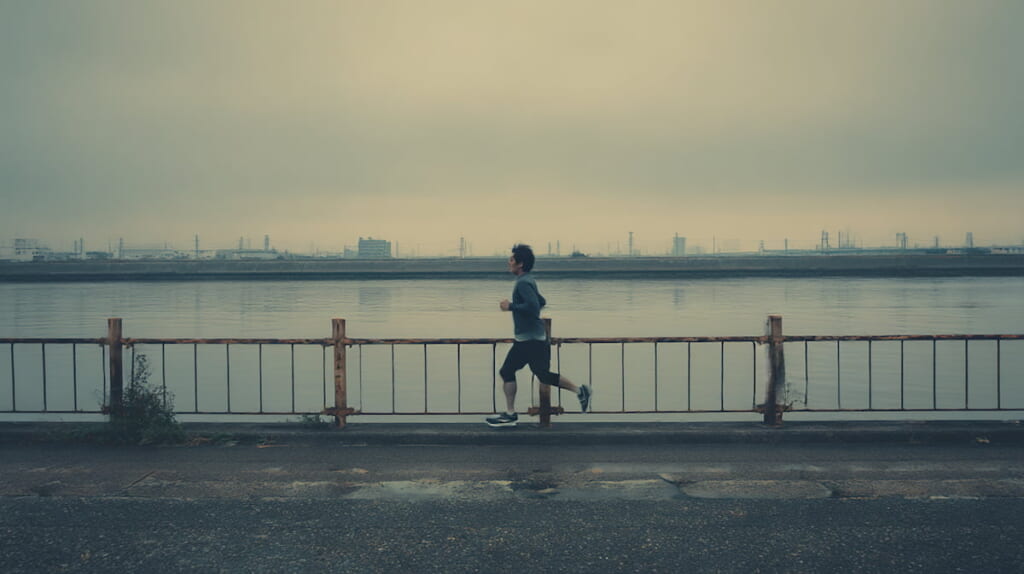40代男性ランナーが朝の川沿いを一人で走っている様子