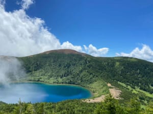 福島の火口湖を望む稜線で、絶景の直後に疲労困憊の表情を見せる日本人男性トレイルランナー